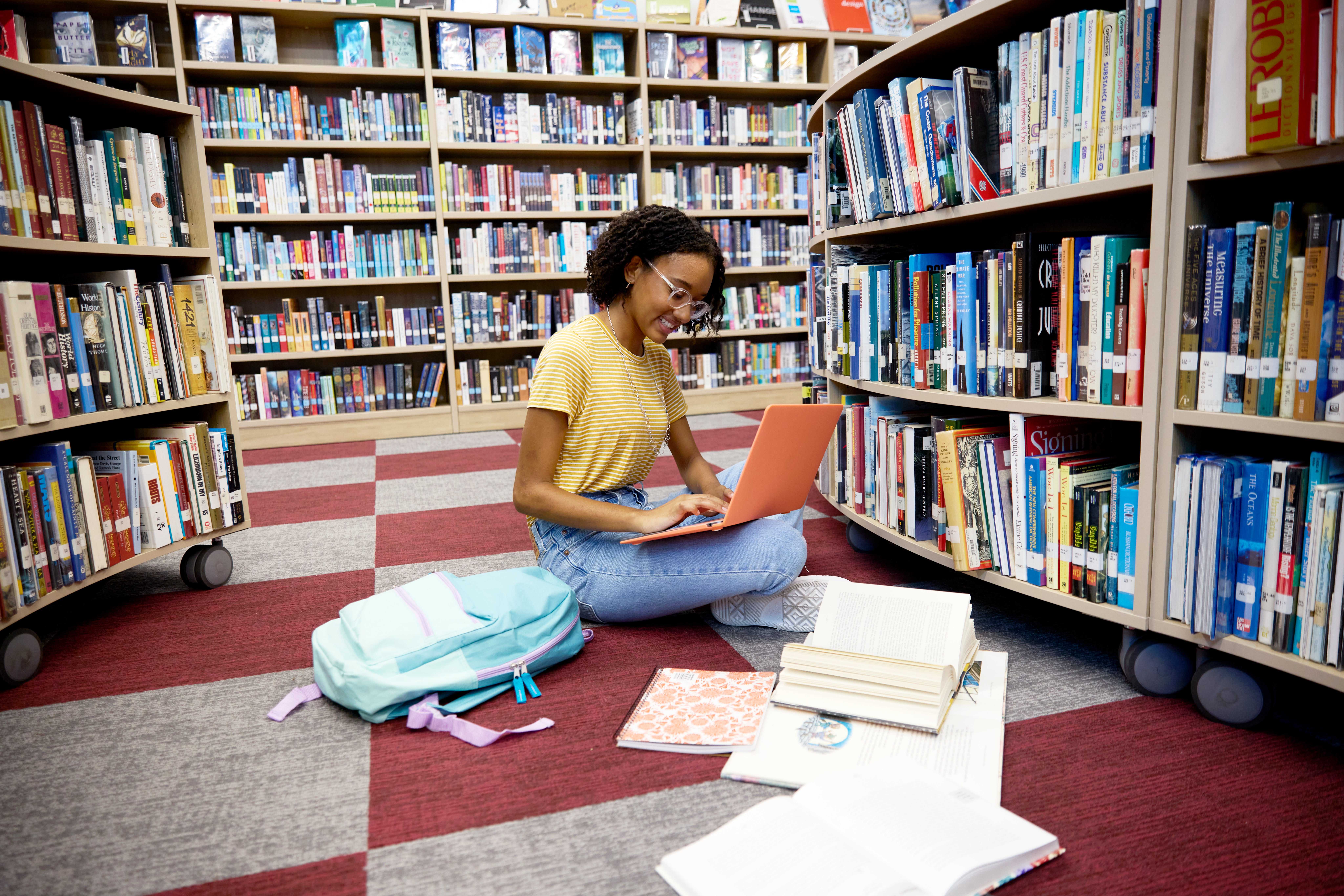 Student sitting on library floor reading a book